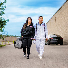 Load image into Gallery viewer, Two people walking outdoors with a clear blue sky and a building in the background.