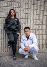 Load image into Gallery viewer, Two people wearing tracksuits against a brick wall.
